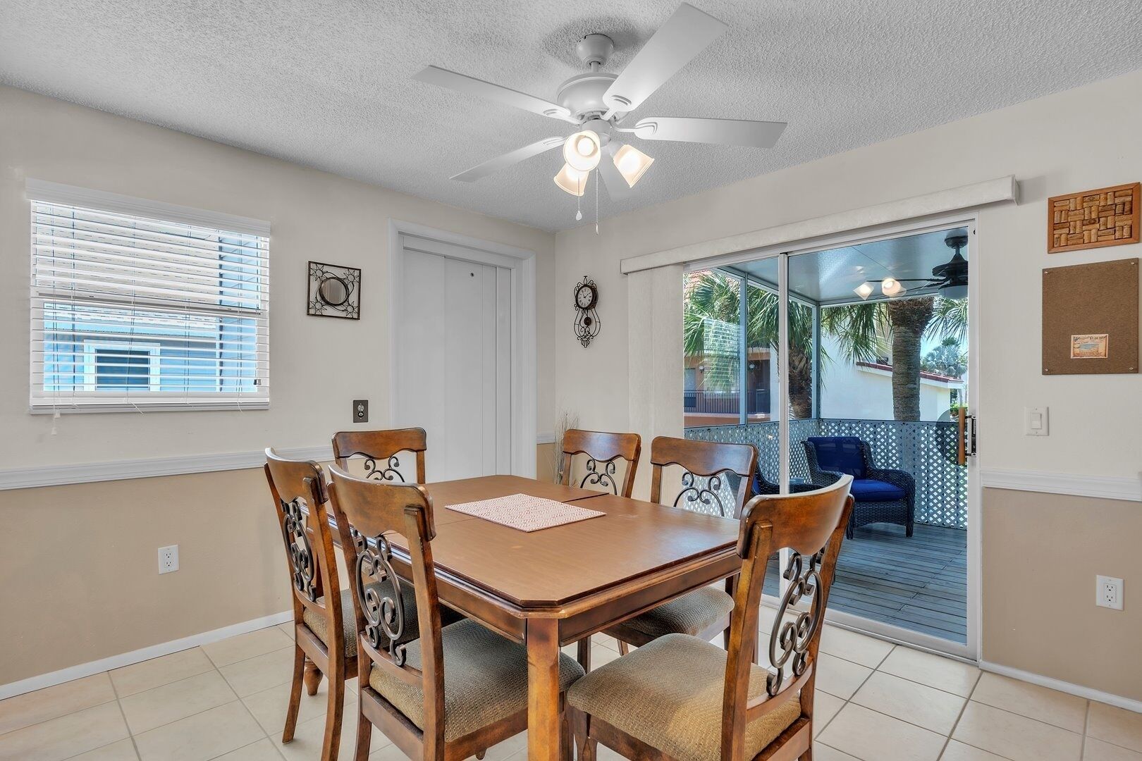 A dining area with a wooden table and chairs, a ceiling fan, and a view of the outdoors through a glass door.