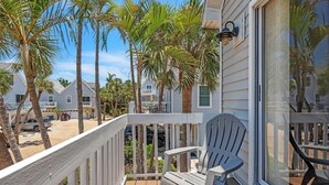 A wooden deck with a white chair, surrounded by palm trees and a beach view. - North Beach Paradise 3 Bedroom Townhouse by RedAwning (Holmes Beach)