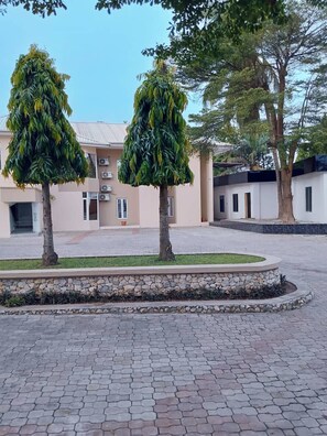A paved courtyard with two trees, a building with air conditioning units, and a stone border. - H31 Royal Classic Apartments  (Lagos)