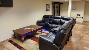 A living room with a leather sofa, a wooden coffee table, and a treadmill in the background.