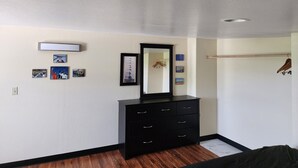 A bedroom with a wooden floor, a black dresser, a mirror, and a clothes rack.
