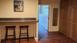 A kitchen with wooden flooring, a granite countertop, two stools, and a framed picture on the wall.