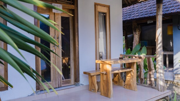 A wooden table and bench set on a tiled patio with a wooden door and window frames. - Kubuyang Cottage (Penida Island)