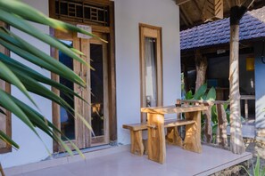 A wooden table and bench set on a tiled patio with a wooden door and window frames. - Kubuyang Cottage (Penida Island)