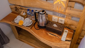 A wooden table with a kettle, cups, water bottles, a tissue box, and a remote control. - Kubuyang Cottage (Penida Island)