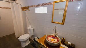 A bathroom with a toilet, a sink with a decorative basin, a mirror, and a towel rack. - Kubuyang Cottage (Penida Island)