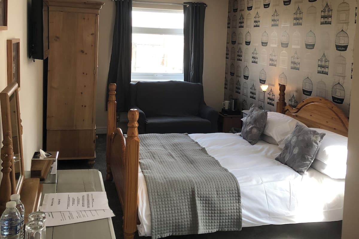 A bedroom with a bed, bedside tables, a wardrobe, a desk with a chair, and a window with curtains.