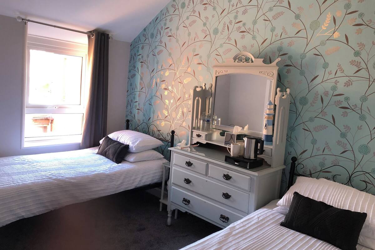 A bedroom with two beds, a dresser, a mirror, and a window with curtains.
