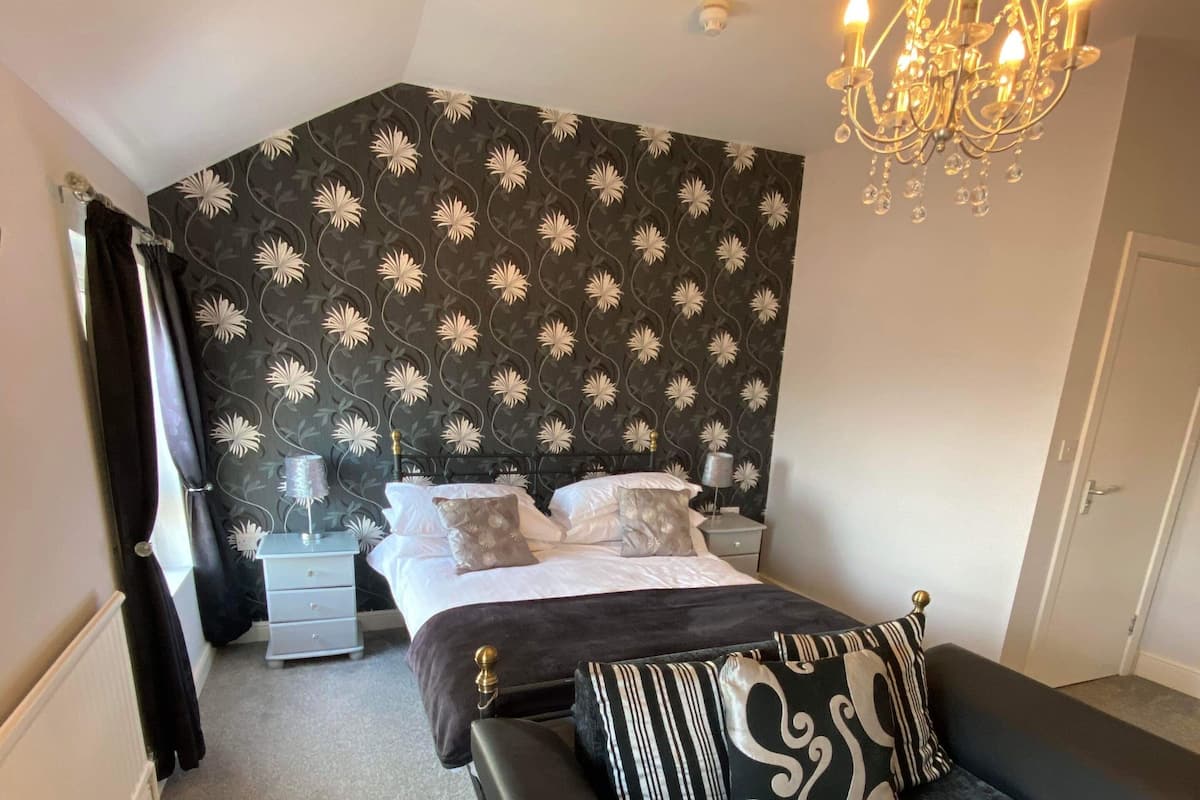 A bedroom with a bed, a sofa, a chandelier, and a patterned wallpaper.