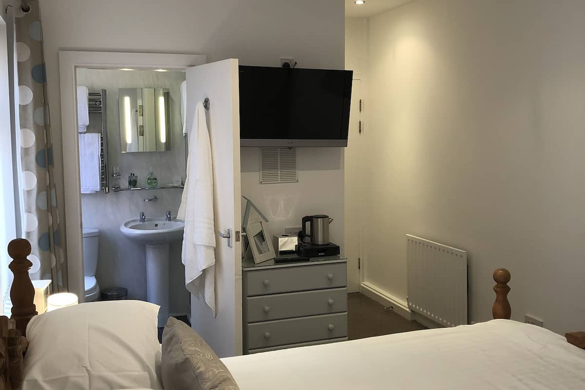 A bedroom with a bed, a dresser, a television mounted on the wall, and a bathroom visible through an open door.