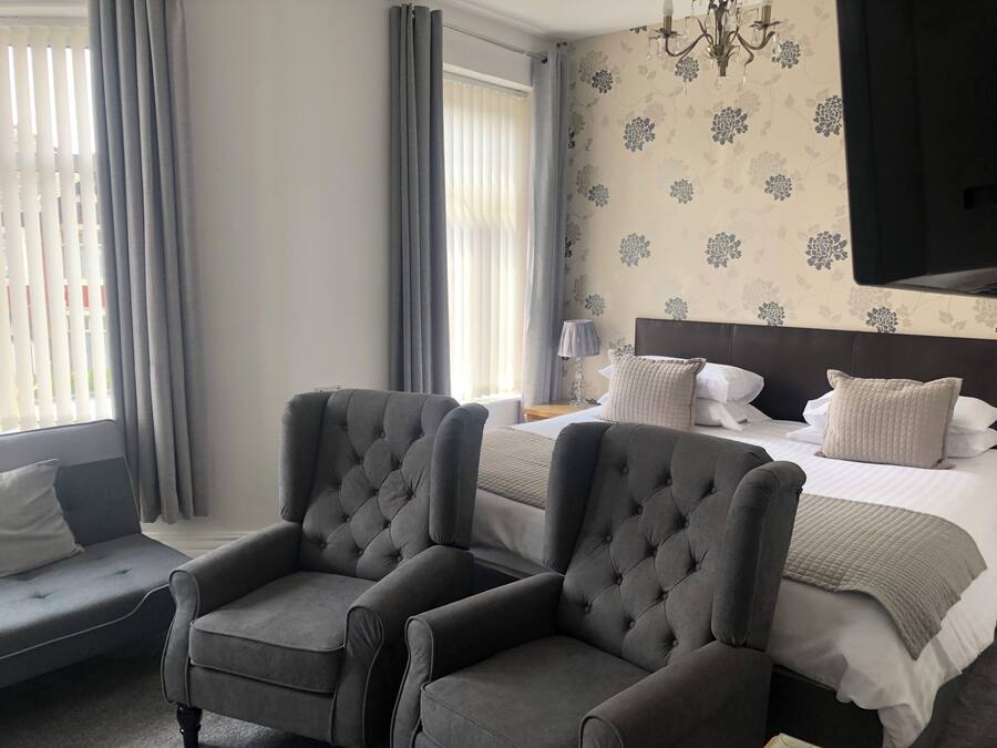 A hotel room with a bed, two armchairs, a nightstand, a lamp, and a wall-mounted TV.