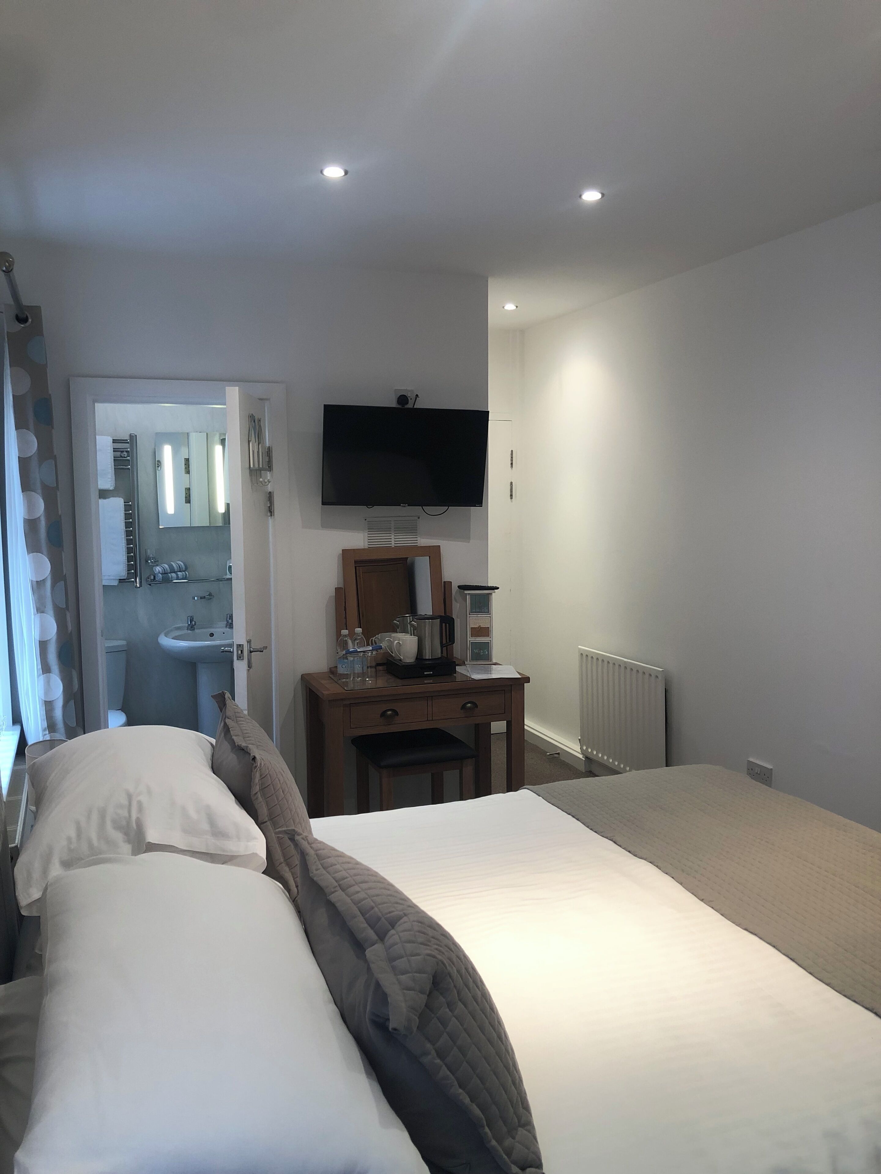 A hotel room with a bed, a desk with a coffee maker, a TV, and a bathroom visible through an open door.