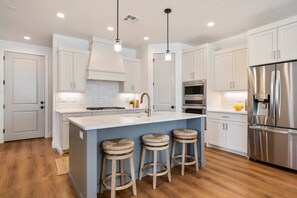 A modern kitchen with white cabinets, a stainless steel refrigerator, a built-in oven, and a central island with stools.