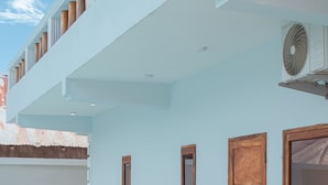 Un edificio moderno con fachada azul claro, escalones de madera que llevan a una entrada con portón, y una unidad de aire acondicionado visible.