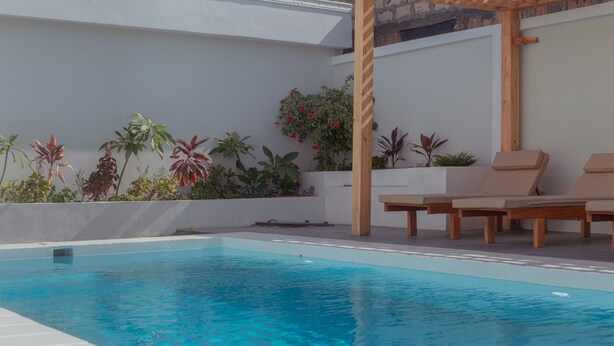 Un área de piscina exterior moderna con sillones de descanso y plantas en macetas.