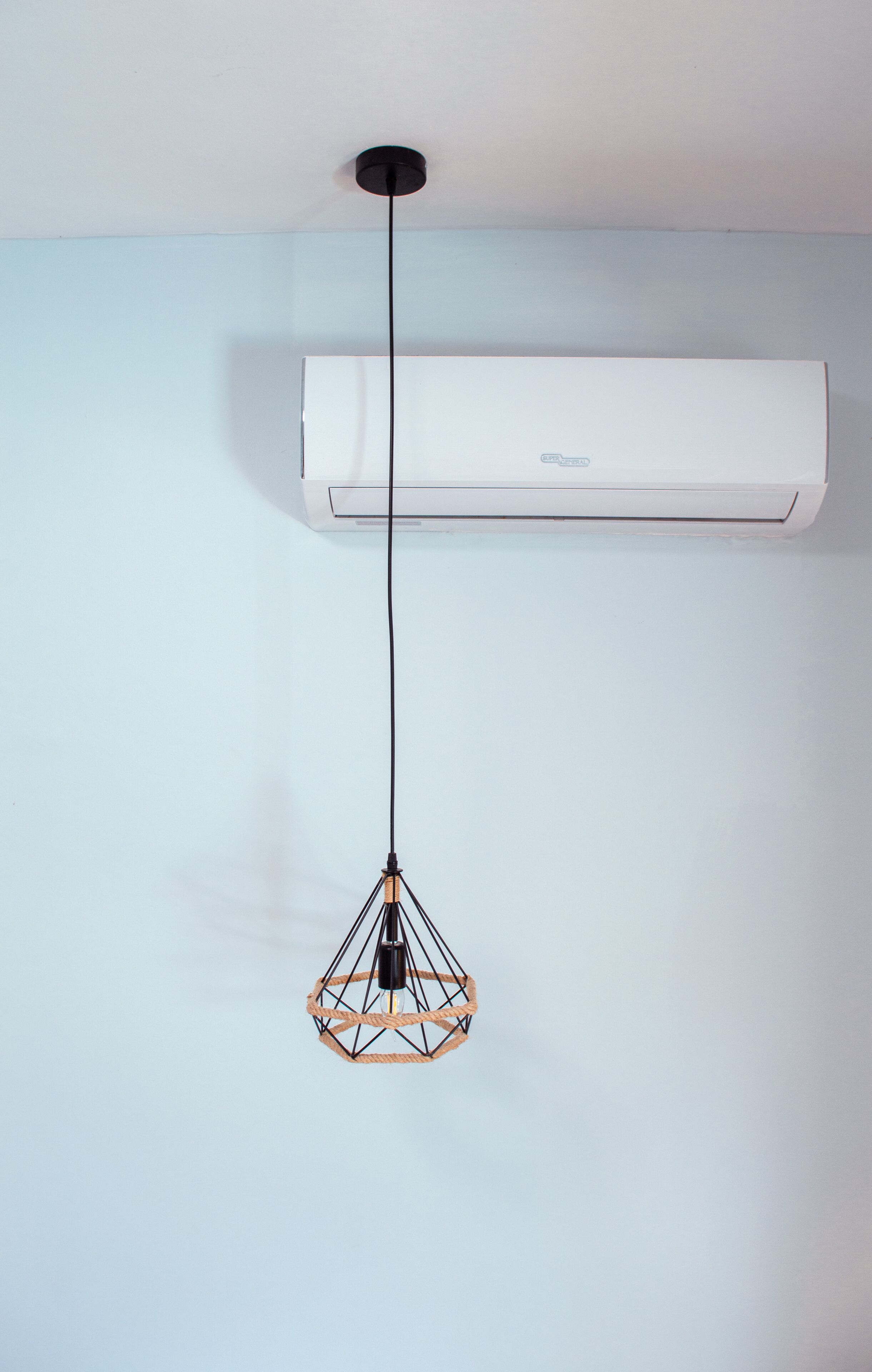 En hvid aircondition-enhed monteret på en lyseblå væg med en sort ledning hængende ned.