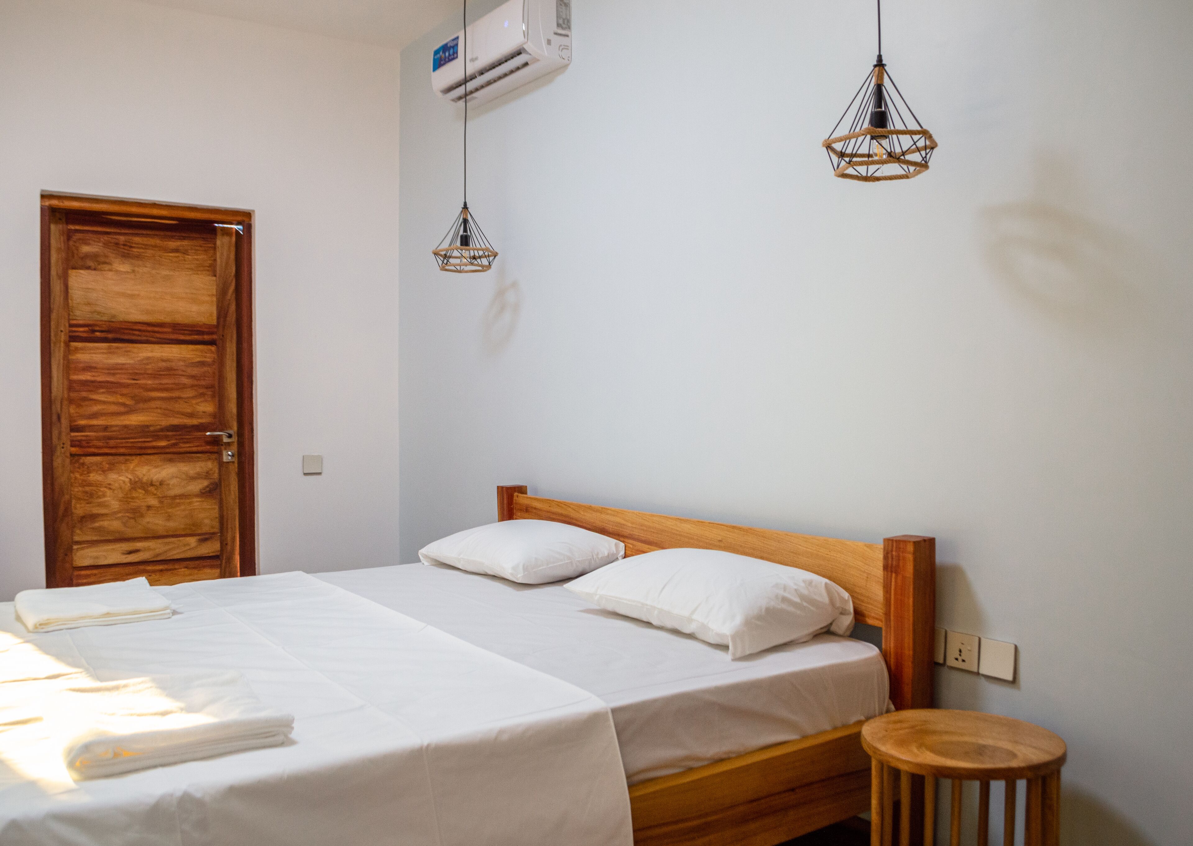 A bedroom with two beds, wooden headboards, white linens, and a wooden stool.