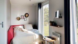 Un dormitorio con cama, una mesita, un televisor y una ventana con cortinas.