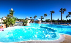 A large outdoor swimming pool with a hot tub, surrounded by palm trees and lounge chairs. - Camping l'Air Marin (Vias)