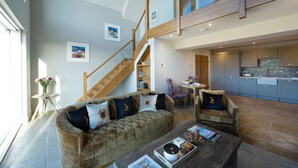Un vaste espace de vie doté d’un haut plafond, d’un escalier en bois, d’une cuisine aux meubles bleus et d’un coin salon confortable avec un canapé et des fauteuils.