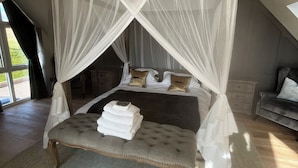 Une chambre à coucher avec un lit à baldaquin, une banquette placée près du lit et une vue sur l’extérieur.