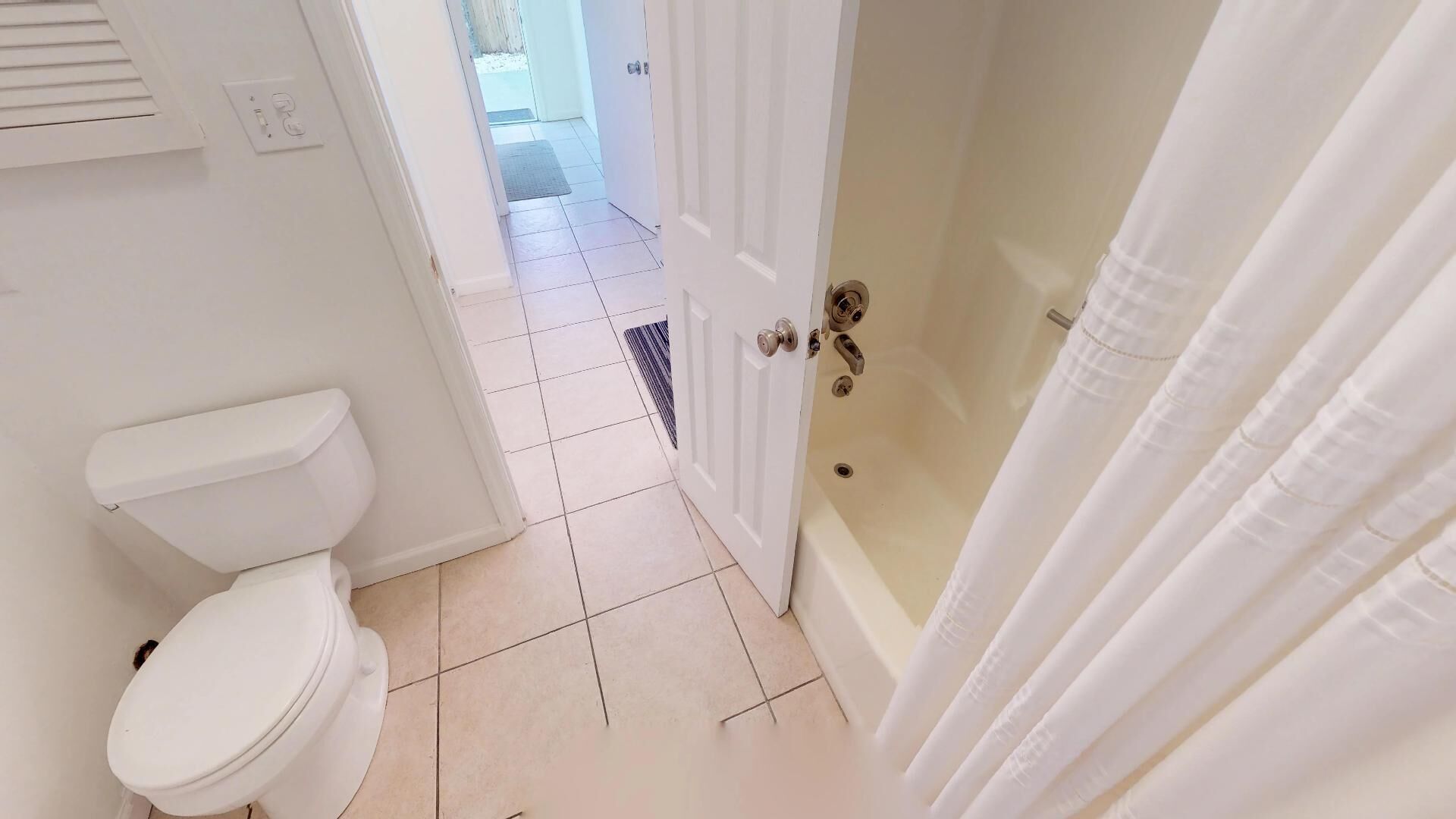 A bathroom with a toilet, a shower with a curtain, and a tiled floor.
