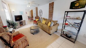 Una sala de estar con un sofá, una mesa de centro, un televisor, muebles de mimbre y una estantería.