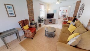 Una sala de estar con sofá, sillones, una mesa de centro, televisor y pared de ladrillo.