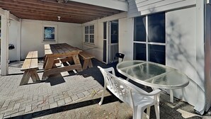 Un patio couvert avec une table et des bancs en bois, une table en verre et une chaise blanche.