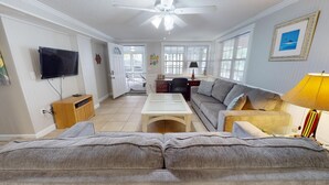 Un salon avec un canapé, une table basse, un téléviseur et un ventilateur de plafond.