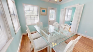Une salle à manger avec une table en verre et des chaises blanches, des murs bleu clair et un plancher en bois.