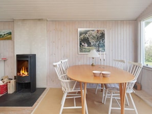 Een gezellige kamer met een open haard, een ronde houten tafel met stoelen, en een lijst met een afbeelding aan de muur.