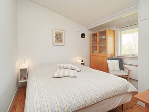 A bedroom with a bed, a wooden cabinet, a chair, and a window.