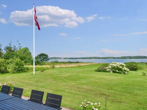 Un drapeau sur un mât, une pelouse avec vue sur un lac et une table avec des chaises.