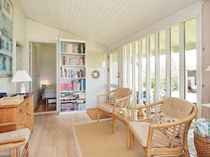 Een gezellige kamer met een boekenkast, rieten meubels en uitzicht door grote ramen.