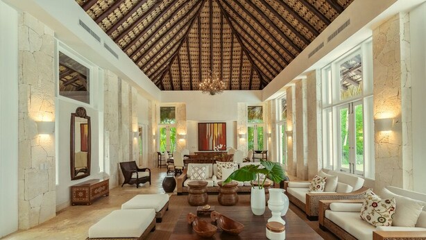 A spacious living room with a high ceiling, large windows, and a central coffee table with decorative items.