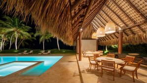 A poolside area with a thatched roof, lounge chairs, and a dining setup.