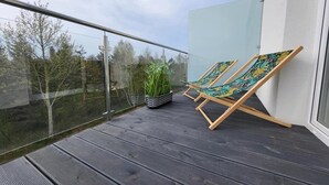 Ein Balkon mit zwei Holzliegen, einem Blumentopf und einem Glasgeländer.