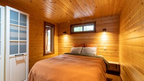 Une chambre dans une cabane en bois, avec un lit, une fenêtre et une porte.