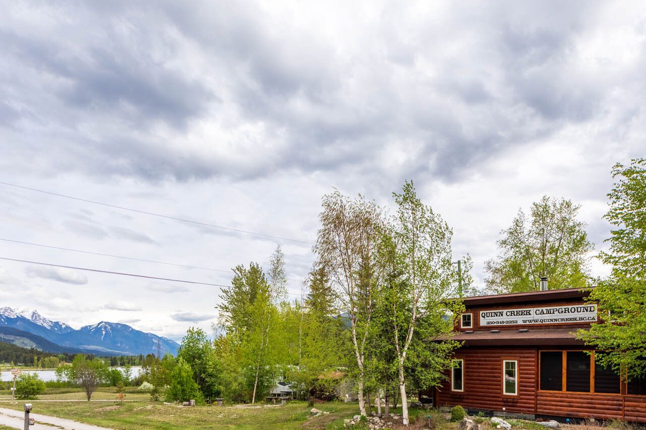 Une cabane en bois portant l’inscription « QUINN CREEK CAMPGROUND », avec vue sur les montagnes et les arbres.