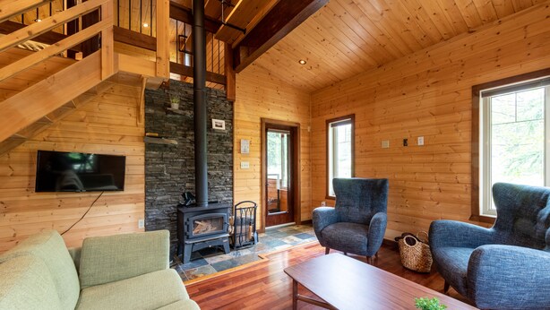 L’intérieur chaleureux d’un chalet en bois, avec une cheminée en pierre, un plancher en bois et un escalier menant à un étage supérieur.