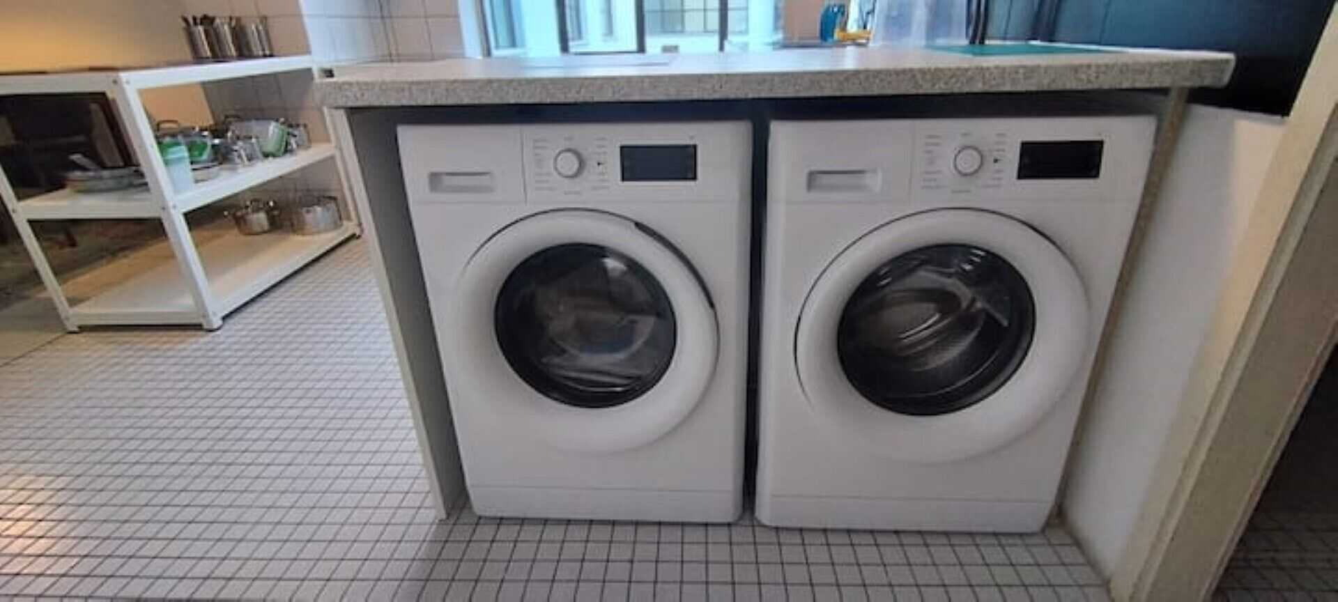 Un espace buanderie compact comprenant deux machines à laver à chargement frontal et un plan de travail au-dessus.