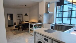 Una cocina compacta con lavadora integrada, un comedor con mesa y sillas, y un ventanal que aporta luz natural.