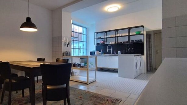 Una cocina moderna con armarios blancos, encimera negra y un comedor con mesa y sillas.