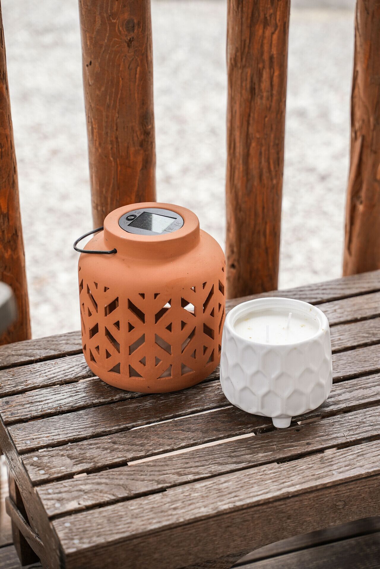 A terracotta lantern with geometric cutouts and a white candle holder on a wooden table.