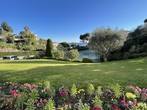 A well-maintained garden with a tennis court, a variety of flowering plants, and a clear blue sky.