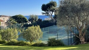 Un court de tennis entouré de verdure, avec vue sur la mer.