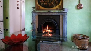 Une pièce avec une cheminée, une table en verre surmontée d’un bol décoratif rouge, un tableau au-dessus de la cheminée et un panier en bois posé sur le sol.