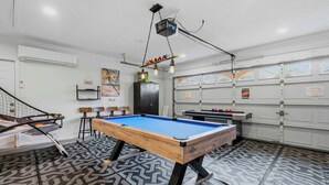 Una mesa de billar en una habitación con alfombra estampada, una mesa de ping pong y una escalera.
