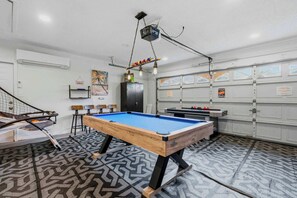 Una mesa de billar en una habitación con alfombra estampada, una mesa de ping pong y una escalera.